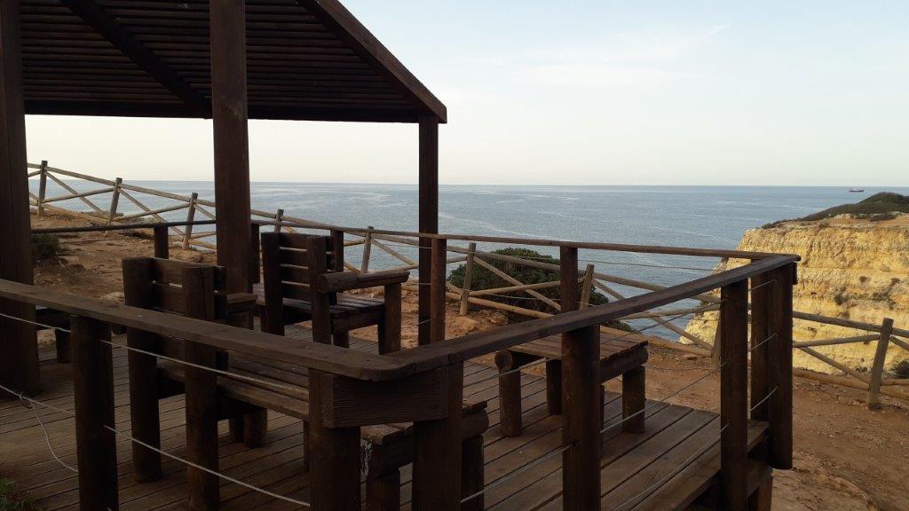 Picknickplaats met houten stoelen en banken met uitzicht over de rotsen en de oceaan, Algarve, Portugal.