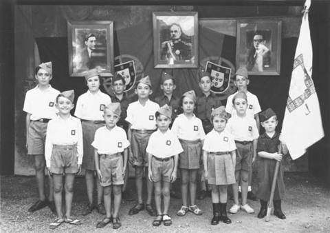 Groep kinderen met baretten en uniformen met op de achtergrond Portugese wapenschilden. 