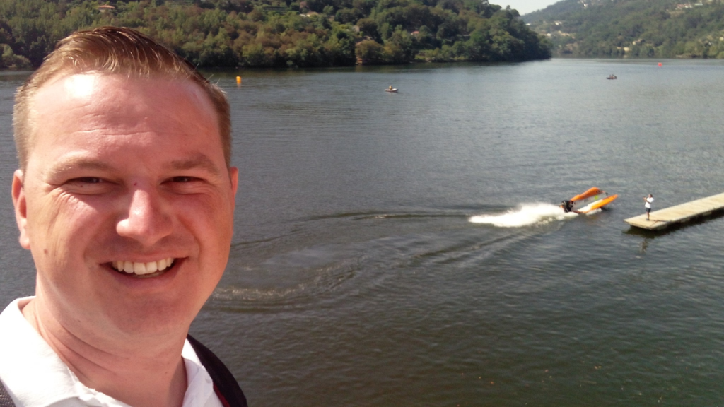 Selfie van Kristof Weckx bij de Dourorivier waar op de achtergrond mensen aan het waterskiën zijn.